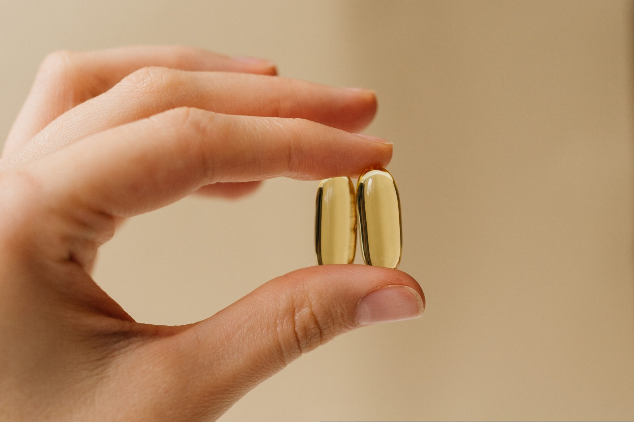 Two,Fish,Oil,Vitamins,Pills,In,Hand,,Clear,Beige,Background