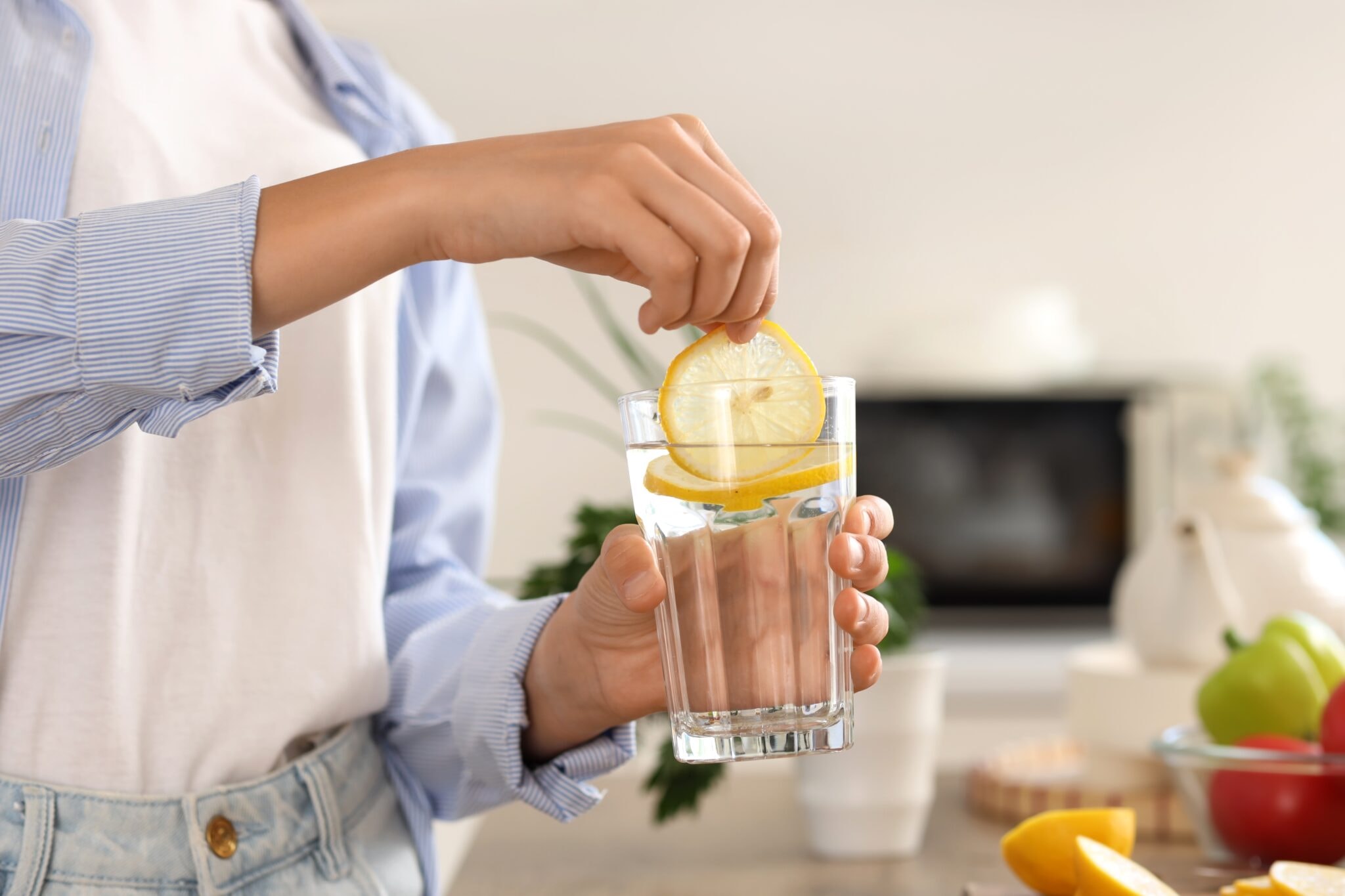 Young,Woman,Putting,Lemon,Slice,Into,Glass,Of,Water,In