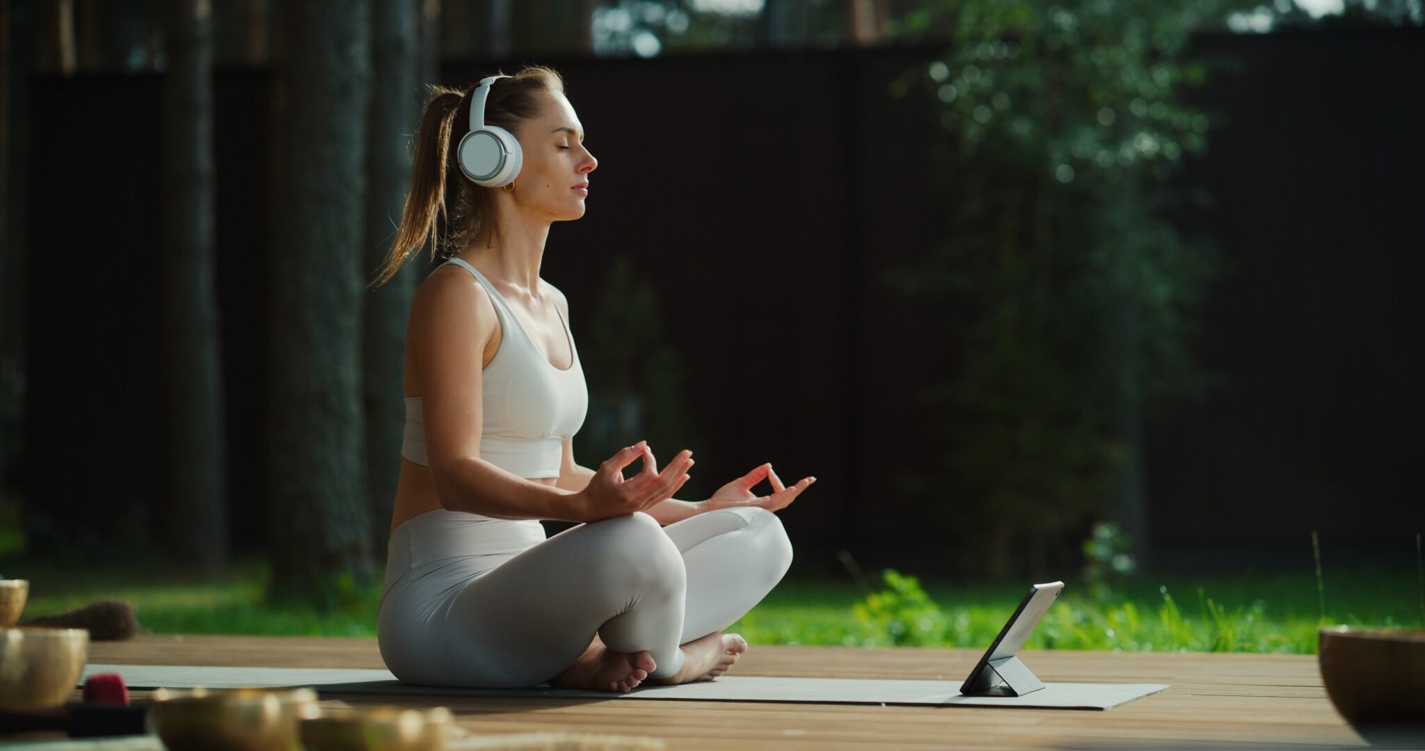 Young,Woman,Sits,Outdoors,,Wearing,Headphones,And,Using,Tablet,For